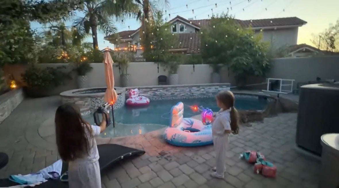 Two kids at dusk playing with glowing Neon Electric Water Blasters near a pool