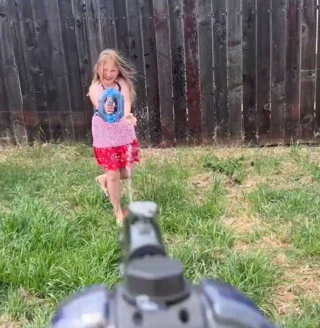 Young girl in a backyard aiming the translucent blue Neon Electric Water Blaster